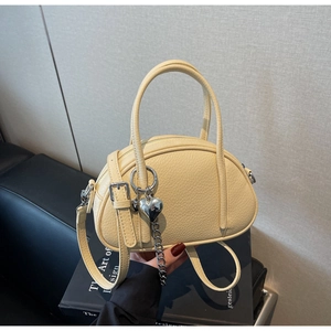 Détail du sac en cuir jaune clair avec pendentif cœur argenté et poignées rondes