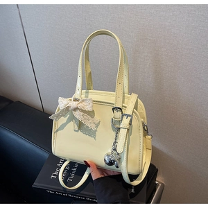 Detail of lemon yellow glossy Boston bag with lace bow and silver bear charm