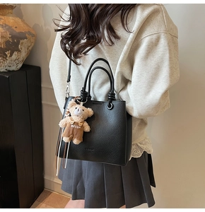 Detail of black lychee grain leather bucket bag with cute bear charm and shoulder strap