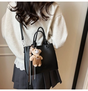 Close-up of black litchi pattern leather tote bag with a cute brown plush bear charm