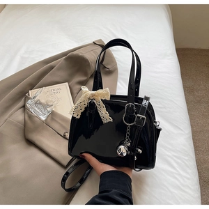 Detail of black patent leather Boston bag with cream lace bow and silver charm