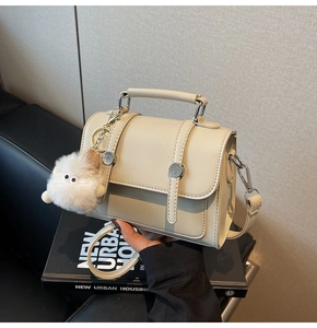 Detailed close-up of a beige faux leather handbag featuring a plush monster charm