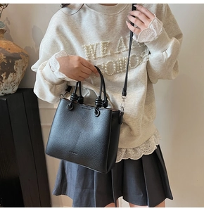 Detail of black lychee texture leather bucket bag with knot handle and metal strap buckle