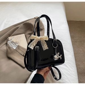 Detail of black patent leather Boston bag with cream lace bow and silver dog charm