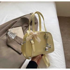Close-up of pale yellow patent leather bag with lace bow and silver dog charm