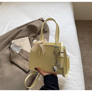 Detail of a pale yellow patent leather Boston bag with lace bow and silver charm