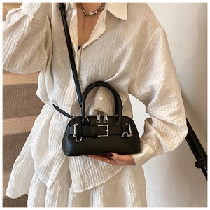 Detail of black leather shell bag with silver buckle and crossbody strap on a model