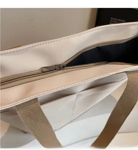 Detail of smooth metal zipper closure and dual front pockets on off-white canvas tote bag