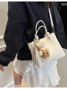 White pebbled leather bucket bag with bear pendant and adjustable crossbody strap