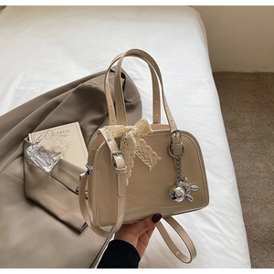 Detail of beige patent leather Boston bag with lace bow and silver balloon dog charm