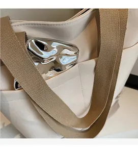 Detail of a beige canvas tote bag showing a durable front pocket with silver metal accessory