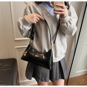 Schwarze glänzende Achseltasche mit goldenen Details, getragen in einem eleganten Raum