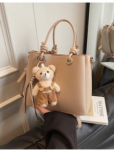 Chic beige lychee textured bucket bag with knotted handles and a cute bear pendant