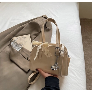 Detail of cream patent leather handbag with lace bow decoration and silver metal charm
