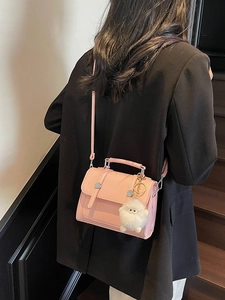 Pink crossbody handbag with plush charm and top handle, styled with a black suit jacket