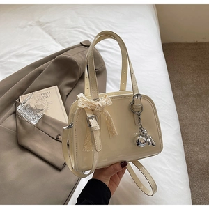 Detail of cream glossy patent leather handbag with lace bow and silver charms