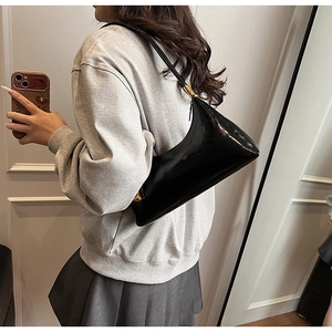 Model trägt eine elegante schwarze Lackleder-Schultertasche mit glänzendem Design