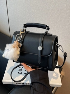 Stylish black rectangular crossbody bag with top handle and plush monster charm