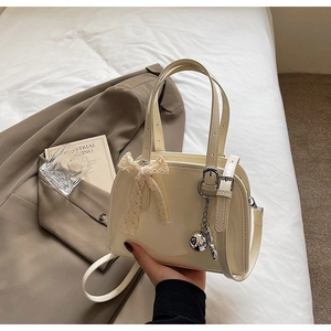 Detail of a beige patent leather Boston bag with lace bow and silver charm on a white bed