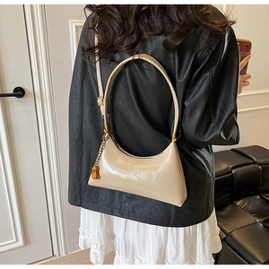 Detail der beigen glänzenden Crescent-Tasche mit goldenem Erdnuss-Anhänger auf Lederjacke