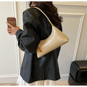 Detailansicht der beigen Lackledertasche mit Goldbeschlägen und metallischem Taschenanhänger