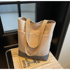 Detail of two-tone beige canvas tote bag with front pocket and good luck patch