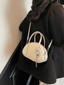 Sac à main chic en cuir crème avec pendentif cœur porté en bandoulière sur blazer