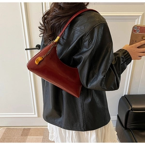 Details einer weinroten Ledertasche mit geometrischem Schnitt und Goldkettchen