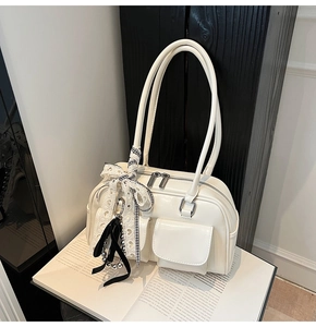 Detalle de bolso brillante crema con bolsillos dobles y colgante de lazo de encaje