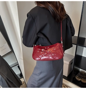 Detail view of a dark red crossbody bag with silver metal studs and buckles on model
