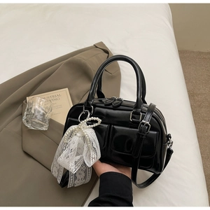 Detail of a black glossy Boston bag featuring front pockets and a pearl lace bow charm