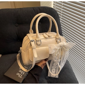 Détail du sac Boston blanc crème avec nœud en dentelle et breloque perle sur siège