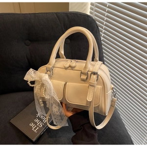 Détail du sac Boston crème avec nœud en dentelle et pendentif en perles sur le côté