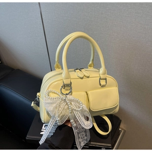 Close-up of yellow glossy leather bowling bag with pearl lace bow charm and silver hardware