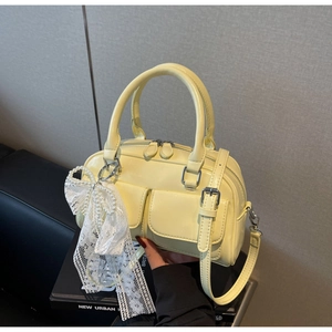 Détail du sac Boston jaune en cuir brillant avec noeud en dentelle et breloque perle
