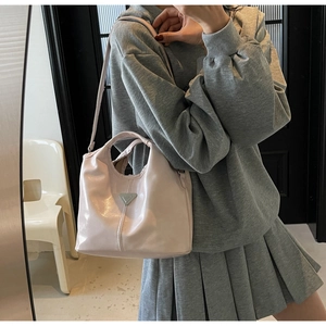 Detail of a shiny pastel pink tote bag featuring a silver triangular metal logo and top handle