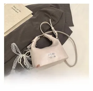 Detailed shot of beige half-moon bag featuring pearl lace charm and metal logo