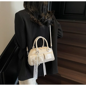 Détail du sac Boston crème avec nœud en dentelle et pendentif en perles