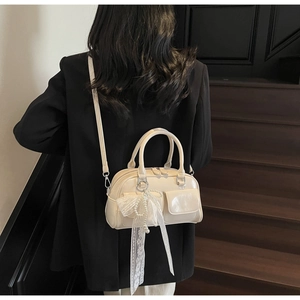 Détail du sac Boston crème avec breloque en dentelle et perles porté par un mannequin