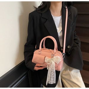 Détail du sac bowling en cuir verni rose avec nœud en dentelle et pendentif en perles