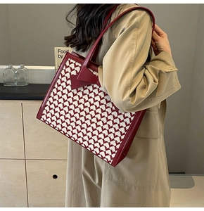 Detail of red houndstooth tote bag with leather bow on a model wearing a beige coat