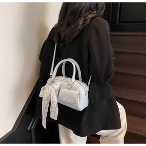 Détail du sac Boston bleu clair avec un nœud en dentelle blanche et charme en perle