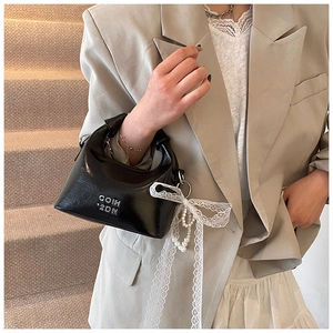 Detail of black glossy leather handbag featuring white lace bow and pearl pendant