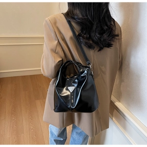 Black glossy bucket bag with silver triangular logo worn by a model in casual attire