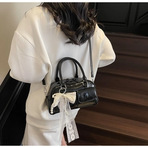 Détail du sac bowling noir brillant avec poches cargo et pendentif nœud en dentelle