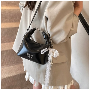 Detail of black patent leather crossbody bag with silver cutout handle and lace pearl charm