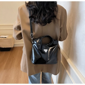 Detailed view of glossy black faux leather shoulder bag with metallic triangle logo detail