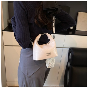 Detail of a creamy beige moon-shaped leather crossbody bag worn by a model in a modern room