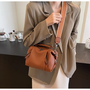 Detail of brown lychee leather Boston bag with stylish orange woven strap and tassels
