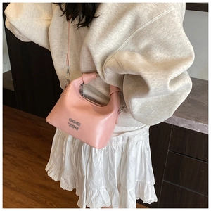 Detailed shot of pink crossbody bag with silver logo worn by model on shoulder